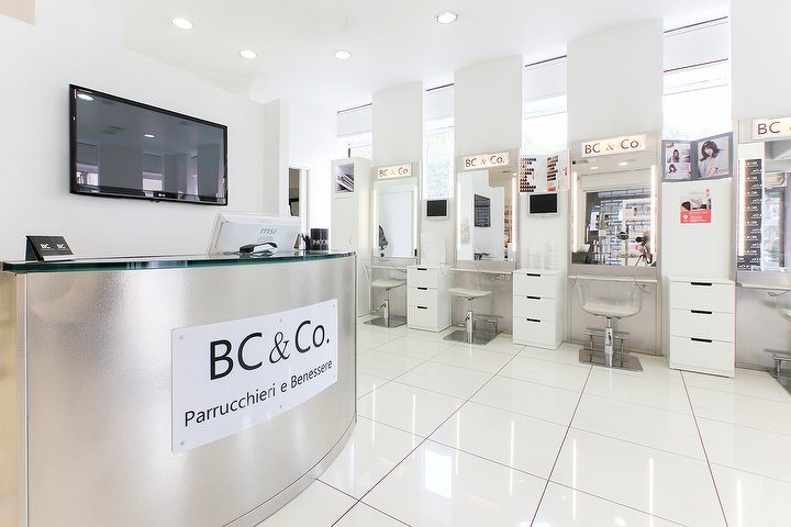 La reception del salone con l'insegna BC & Co. Parrucchieri e Benessere e le postazioni bianche sullo sfondo
